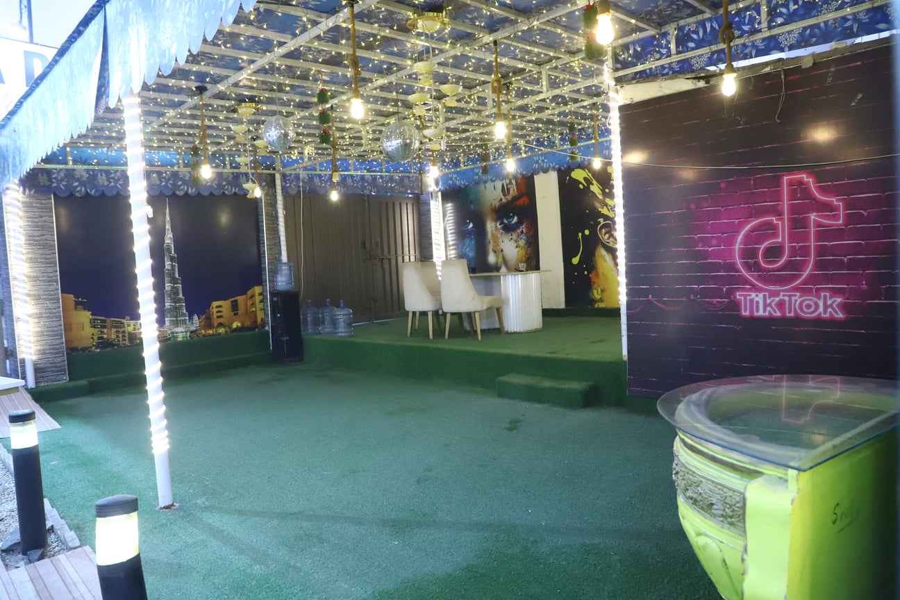 outdoor lounge area featuring string lights, green turf, and a neon TikTok sign.